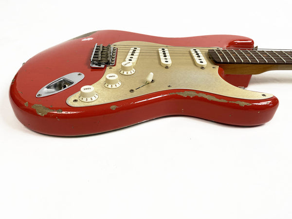 Red electric guitar with a worn and chipped finish, white pickguard, three single-coil pickups, and tone and volume knobs on a white background