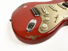 Close-up of red electric guitar body with vintage wear and chips, showing volume and tone knobs, input jack, and pickups on white background