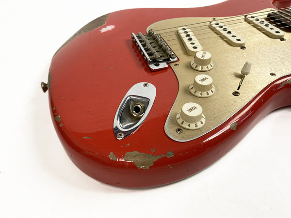 Close-up of red electric guitar body with vintage wear and chips, showing volume and tone knobs, input jack, and pickups on white background