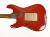 Back of worn red Fender Stratocaster electric guitar showing relic finish and metal neck plate with serial number, against white background