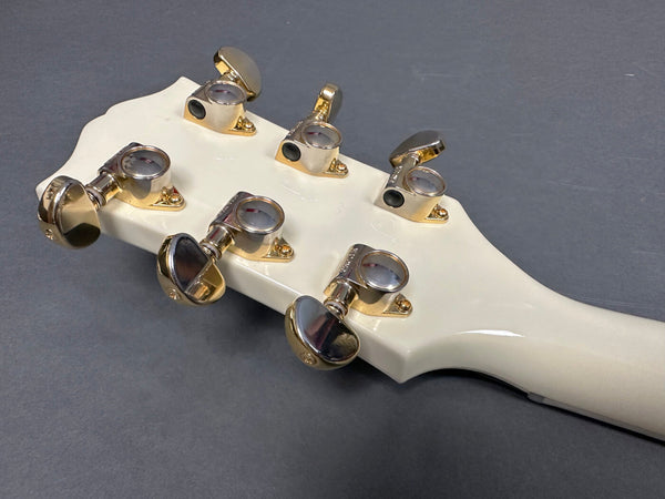 Close-up of white guitar headstock with gold tuning pegs on gray background