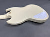 Back view of cream-colored electric guitar body with white control cavity cover and gold strap button on gray background