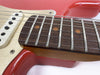 Close-up of red electric guitar neck and fretboard with metal frets, dot inlays, and strings next to white pickup and cream pickguard