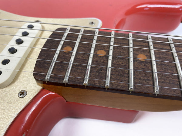 Close-up of red electric guitar neck and fretboard with metal frets, dot inlays, and strings next to white pickup and cream pickguard