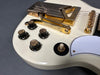 Close-up of white electric guitar with gold hardware, black control knobs, and toggle switch for rhythm and treble settings on dark background