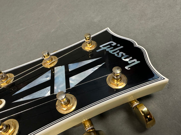 Close-up of Gibson guitar headstock with mother-of-pearl inlay and gold tuning pegs on gray background