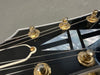 Close-up of black guitar headstock with mother-of-pearl inlay and gold tuning pegs, detailed strings on Coffee House Guitars product listing