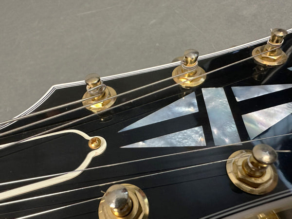 Close-up of black guitar headstock with mother-of-pearl inlay and gold tuning pegs, detailed strings on Coffee House Guitars product listing