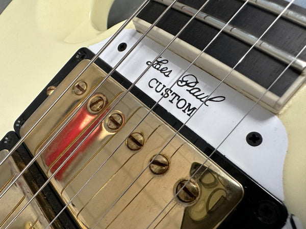 Close-up of cream Les Paul Custom electric guitar with gold humbucker pickups and black-bordered white pickup ring