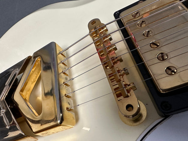 Close-up of white electric guitar bridge and gold-plated pickup cover with six strings and adjustable saddles at Coffee House Guitars.