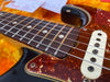 Close-up of electric guitar rosewood fretboard, steel strings, tortoiseshell pickguard, and single-coil pickup in a guitar case with orange plush interior