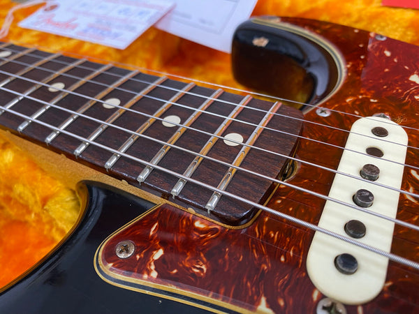 Close-up of electric guitar rosewood fretboard, steel strings, tortoiseshell pickguard, and single-coil pickup in a guitar case with orange plush interior