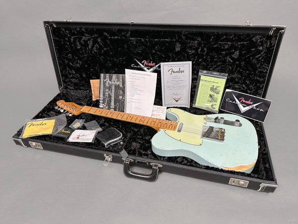 Fender Custom Shop vintage style light blue electric guitar with maple fretboard in open black hard case surrounded by Fender authenticity certificate, manuals, and accessories on gray background