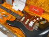 Vintage black Fender Stratocaster electric guitar with tortoiseshell pickguard, three single-coil pickups, worn finish, and Fender owner's manual inside plush orange guitar case