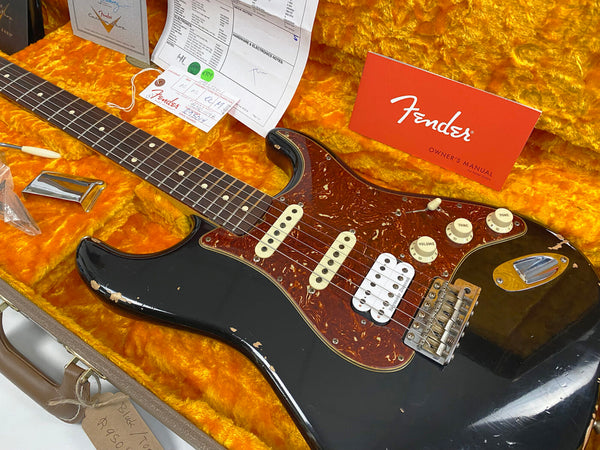 Vintage black Fender Stratocaster electric guitar with tortoiseshell pickguard, three single-coil pickups, worn finish, and Fender owner's manual inside plush orange guitar case