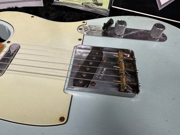 Close-up of vintage Fender electric guitar bridge, pickup, and control knobs on light blue body with cream pickguard.