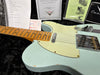 Close-up of vintage Fender Telecaster electric guitar in light blue with maple fretboard, showing signs of wear and oxidation on hardware, laid on black plush surface with Fender documentation and setup checklist in the background.