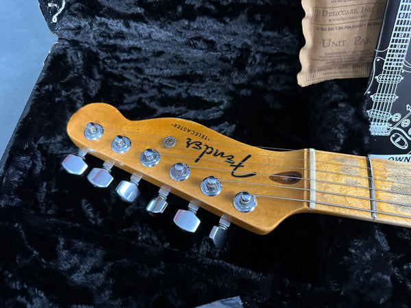 Close-up of Fender Telecaster guitar headstock with tuning pegs, maple neck, and Fender logo on black plush case interior