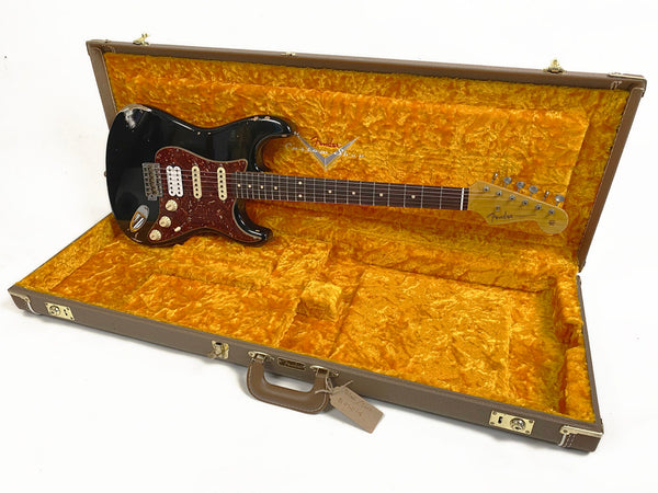 Vintage black Fender Stratocaster electric guitar with tortoiseshell pickguard in open brown Fender hard case with orange plush interior