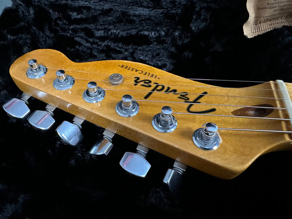 Close-up of Fender Telecaster electric guitar headstock with tuning pegs and strings on black plush surface