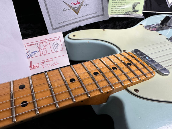 Close-up of light blue Fender electric guitar maple neck and fretboard with black dot inlays and certification cards from Fender Custom Shop in the background