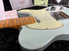 Close-up of vintage Fender Telecaster electric guitar with light blue finish, maple neck, and aged pickguard showing wear and patina, photographed on black plush surface with Fender certificate and paperwork in background.