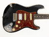 Black electric guitar with tortoiseshell pickguard and white humbucker and single-coil pickups, worn vintage style with visible paint chips and scratches, close-up view of body and neck on white background.