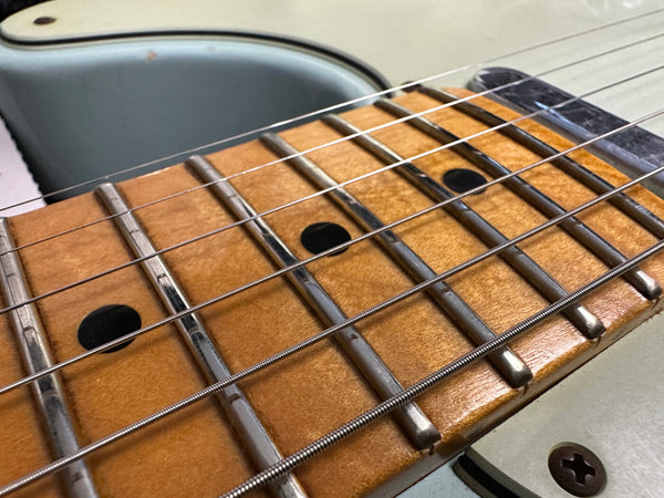 Close-up of electric guitar fretboard with metal frets and strings on a light blue body guitar from Coffee House Guitars