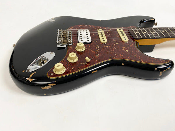 Black electric guitar with tortoiseshell pickguard, three pickups including a white humbucker, and cream tone and volume knobs with visible wear and scratches on the body.