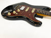 Black electric guitar with tortoiseshell pickguard and cream control knobs, vintage wear and finish chips visible on body edges, maple neck with rosewood fretboard