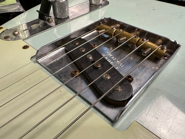 Close-up of vintage electric guitar bridge and single-coil pickup with metal saddle and steel strings on light blue guitar body