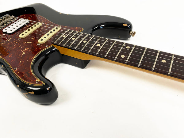 Black electric guitar with tortoiseshell pickguard, worn finish, rosewood fretboard, and three single coil pickups on white background
