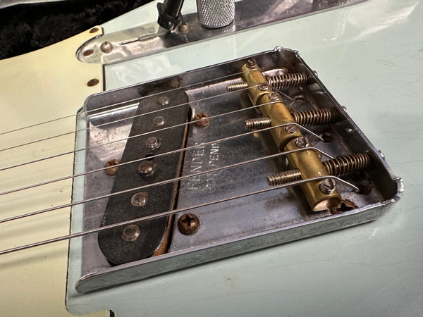 Close-up of vintage Fender Telecaster bridge with brass saddles and steel strings on light blue guitar body