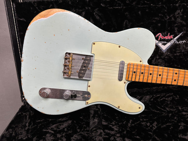 Close-up of vintage Fender Telecaster electric guitar with worn light blue finish and maple fretboard resting in black plush Fender custom shop case