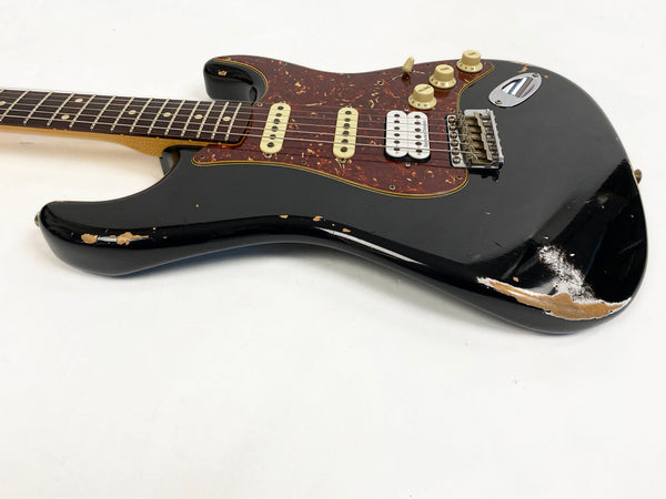 Black electric guitar with tortoiseshell pickguard, three pickups including one humbucker, and visible wear and paint chipping on body edges, photographed on white background.