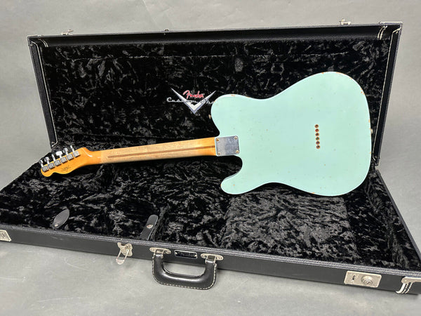 Back of vintage Fender electric guitar in surf green finish with maple neck shown in open black plush-lined Fender Custom Shop hard case on gray background