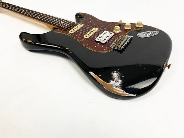 Black electric guitar with tortoiseshell pickguard, three pickups including one humbucker, and visible wear on the body showing wood underneath