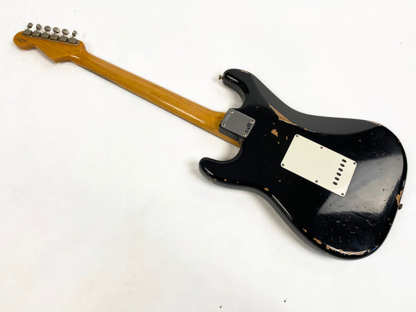 Black electric guitar with wooden neck and vintage wear and tear on body, back view on white background