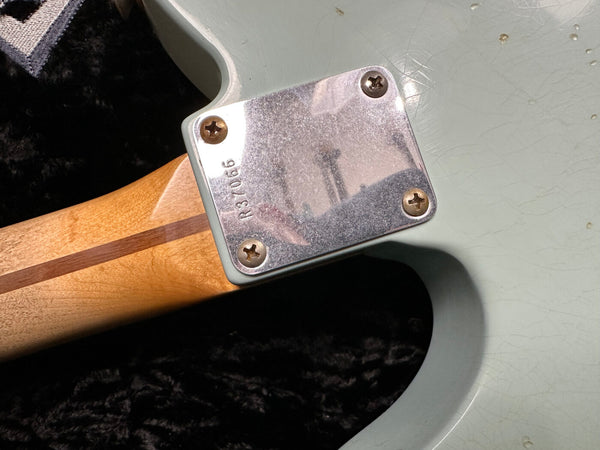 Close-up of electric guitar neck plate with serial number R37066, showing wood neck and light-colored guitar body on black background.