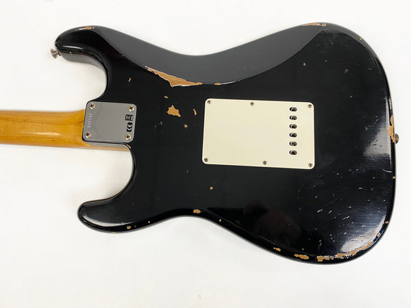 Black electric guitar body with visible wear and paint chipping, maple neck, and white backplate on a white background