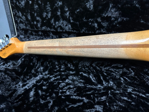 Close-up of guitar neck with skunk stripe wood design resting on black plush guitar case interior