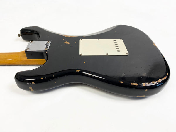 Black electric guitar body with visible wear and paint chipping, showing back side with white pickup cover and wooden neck attached, photographed on white background
