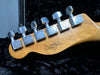 Close-up of Fender Custom Shop guitar headstock with chrome tuning pegs on natural wood finish against black plush guitar case lining