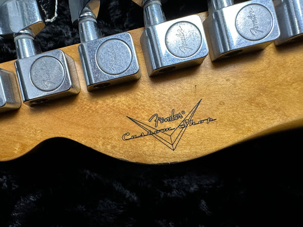 Close-up of Fender Custom Shop guitar tuning pegs and logo on natural wood neck headstock against black background