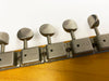 Close-up of vintage guitar tuning pegs with metal tuning machines on light wood headstock against white background
