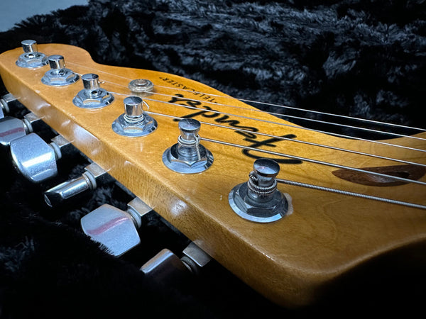 Close-up of Fender Telecaster guitar headstock with tuning pegs and strings on black plush background