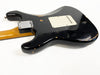 Back view of black electric guitar with worn finish and maple neck shown on white background