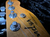 Close-up of Fender Telecaster guitar headstock with tuning pegs and strings on black background