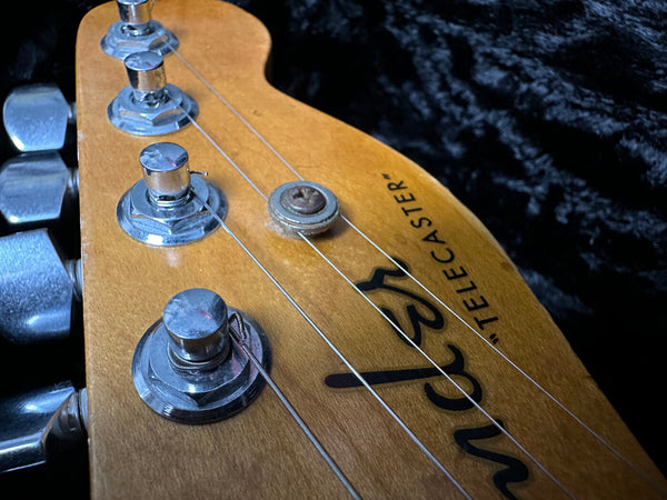 Close-up of Fender Telecaster guitar headstock with tuning pegs and strings on black background