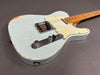 Close-up of vintage light blue electric guitar with distressed paint and maple neck on gray background